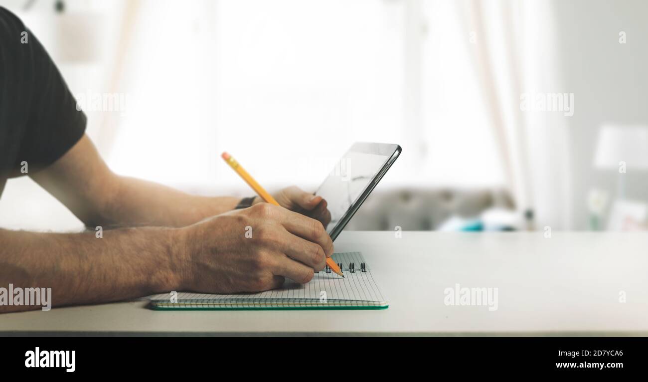 man using digital tablet and writing in note book at home. online learning, distance education and studying concept Stock Photo