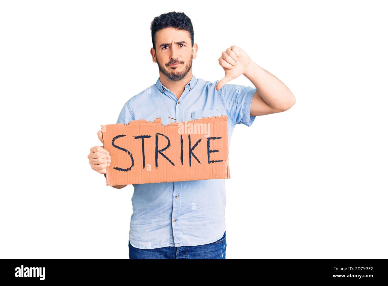 Young hispanic man holding strike banner cardboard with angry face, negative sign showing dislike with thumbs down, rejection concept Stock Photo