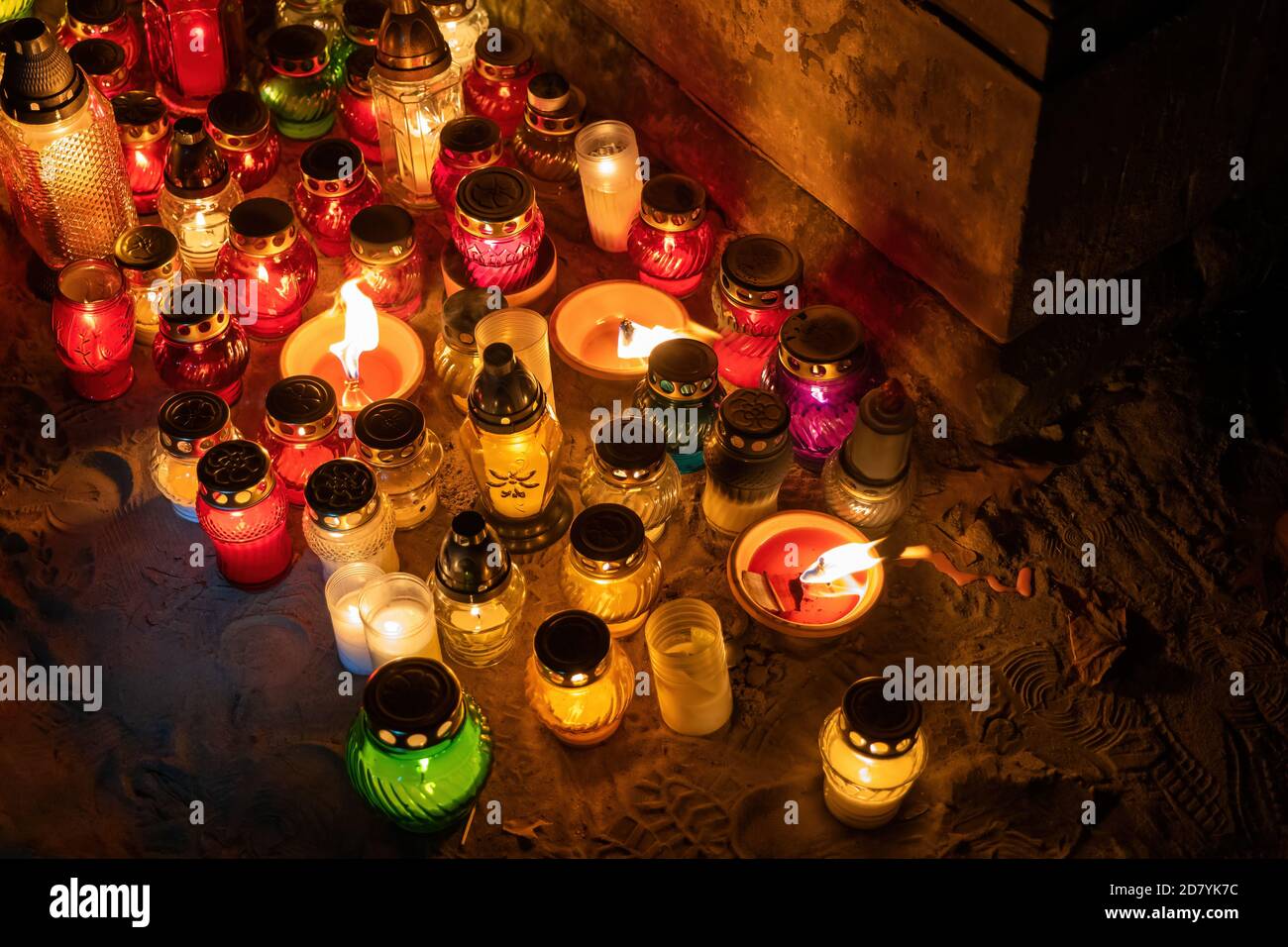Candle lights at night on the ground below a tomb in a cemetery on All