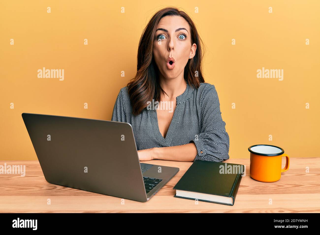 Young brunette woman working using computer laptop scared and amazed ...