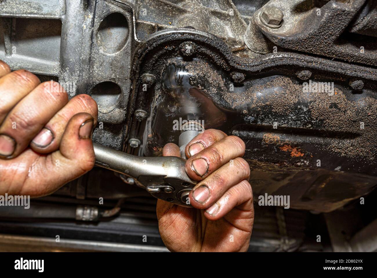 The car mechanic bolts a new screw with a copper washer to the oil sump