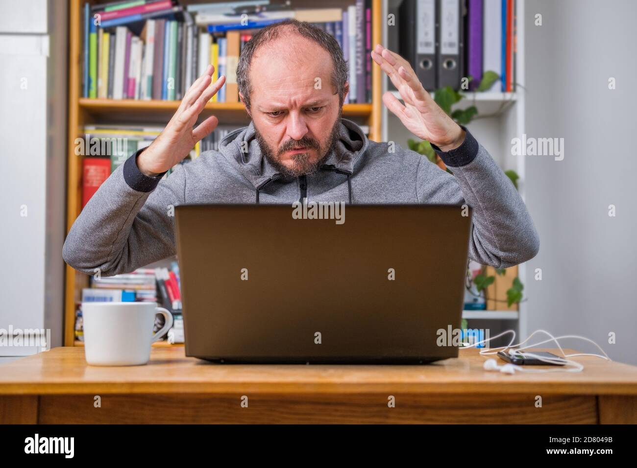 Angry man working online from home office on computer laptop behind vintage desk, arms gesture, business problem concept Stock Photo