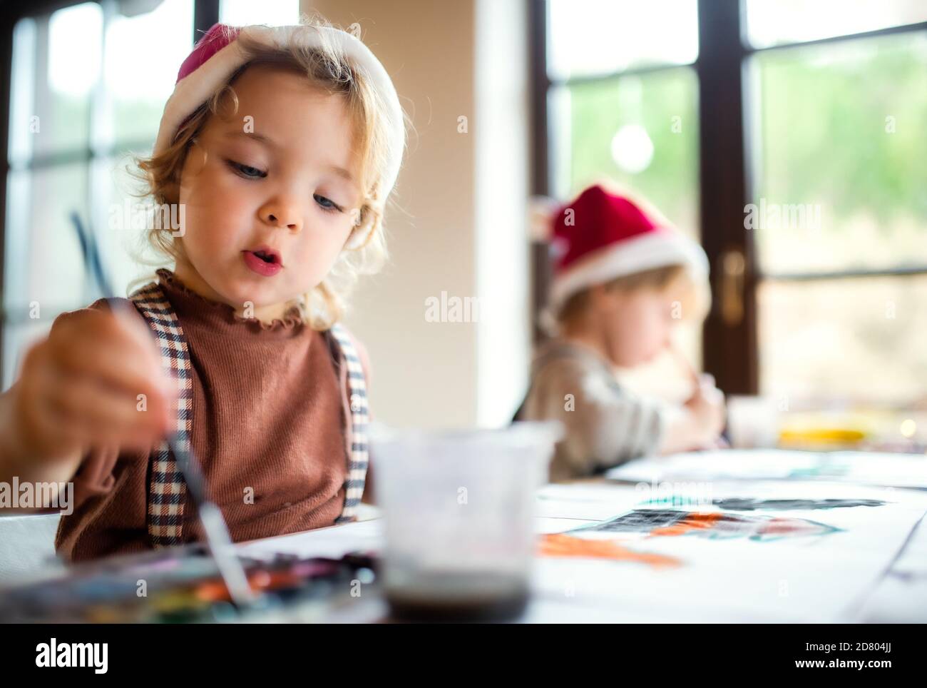 Portrait of small girl and boy indoors at home at Christmas, painting pictures. Stock Photo