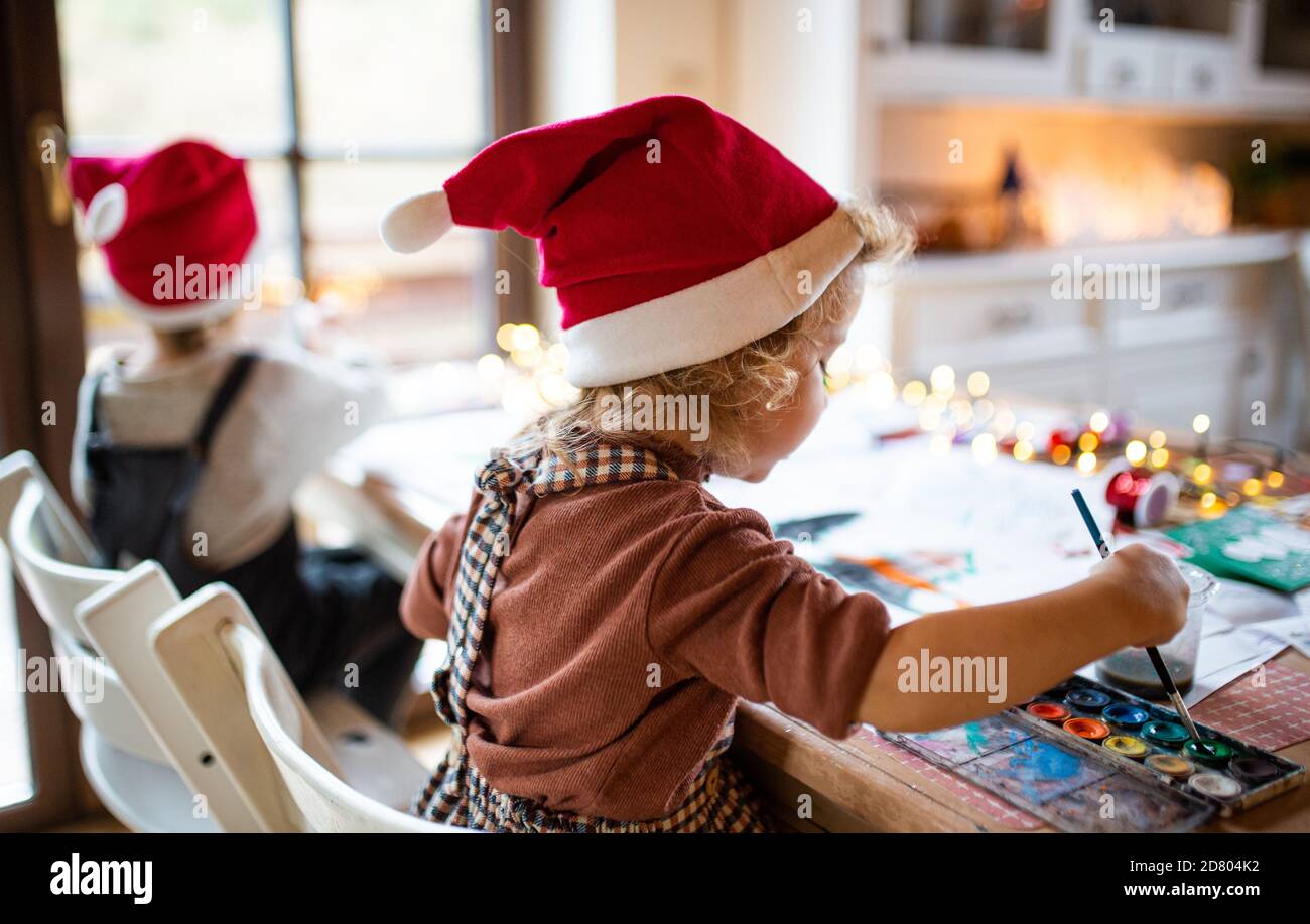 Rear view of small girl and boy indoors at home at Christmas, painting pictures. Stock Photo