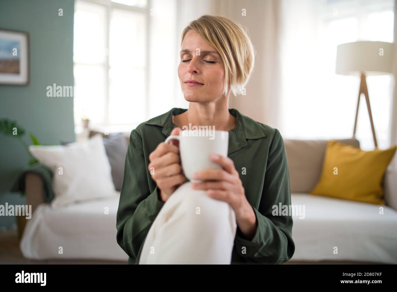 Portrait of woman meditating indoors in office, holding cup of tea. Stock Photo
