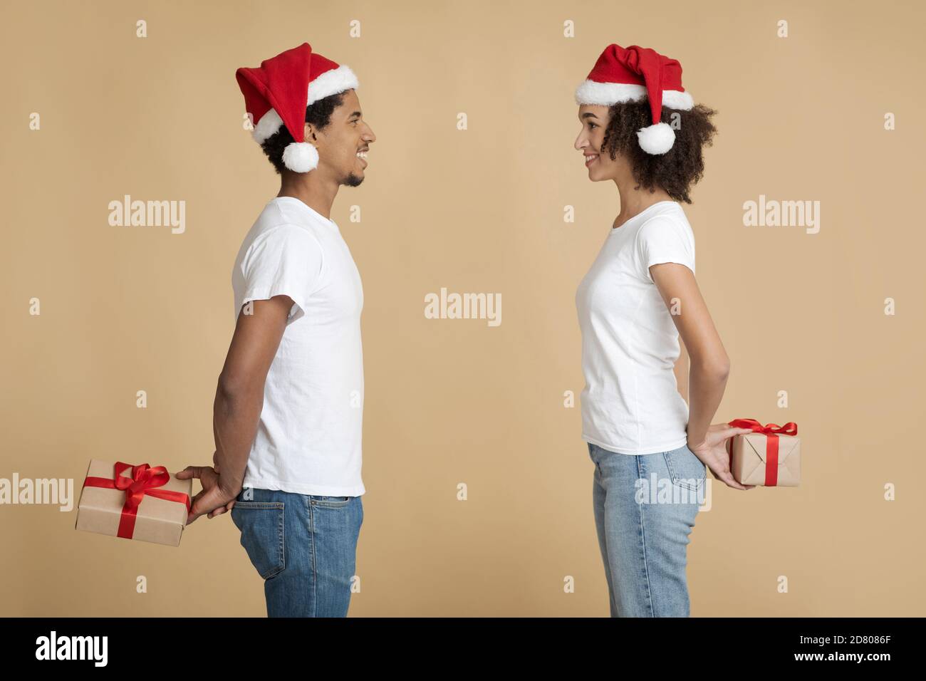 Smiling young man and woman in Santa Claus hats look at each other and ...
