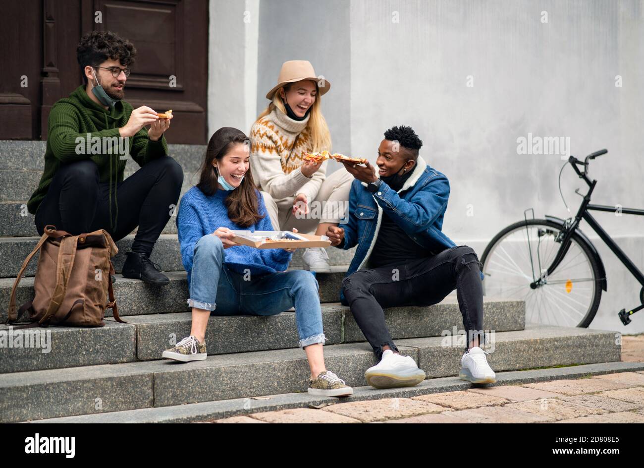 Group of young people outdoors in town, eating pizza. Coronavirus concept. Stock Photo