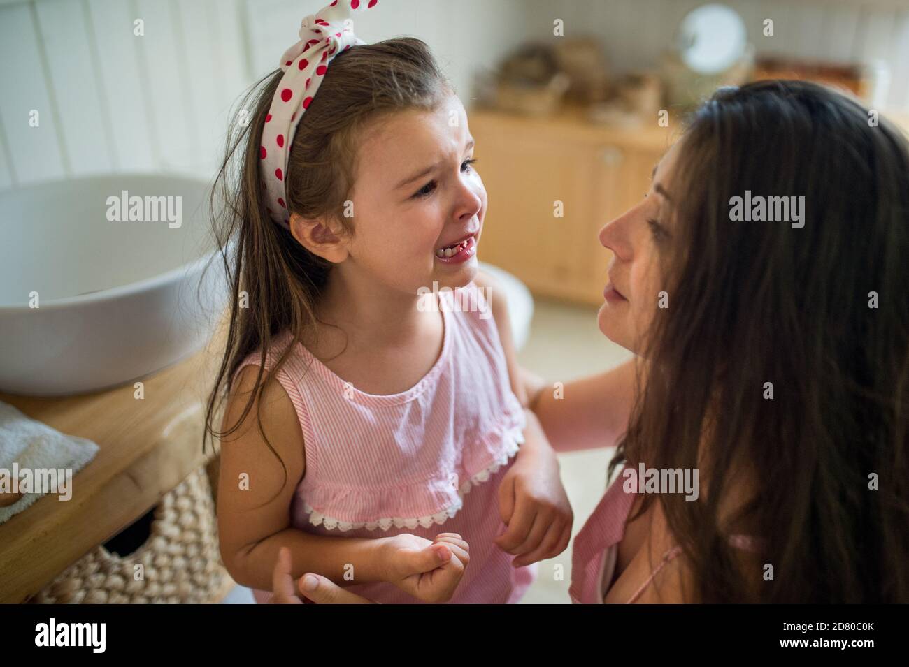 Crying small girl with mother indoors, loosing baby tooth. Stock Photo