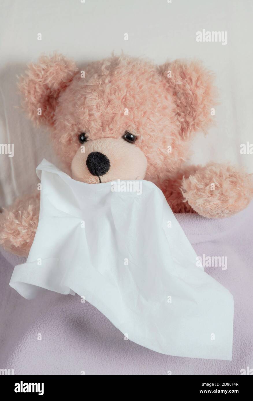 Cold, flu or allergy in kids. Cute teddy in bed sneezing, holding a