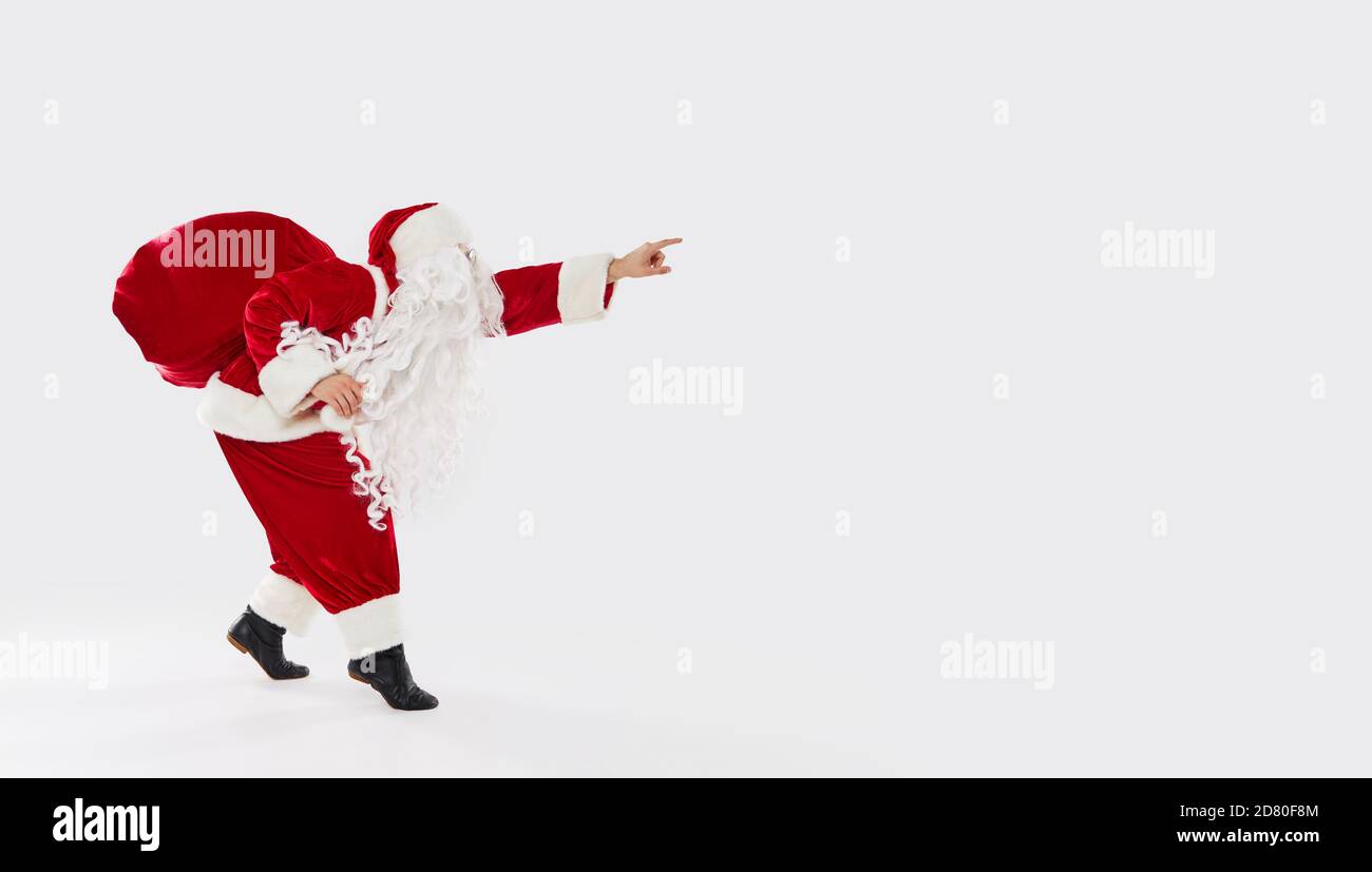 Joyful Santa walks widely with a bag of gifts on his back on a white ...