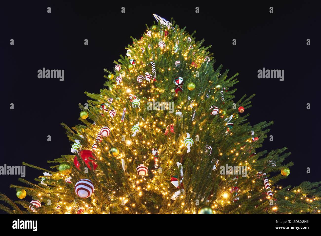 Beautiful Christmas Tree decorated with garlands, Christmas candies and different colorful baubles. New Year decorations. Black background. Stock Photo