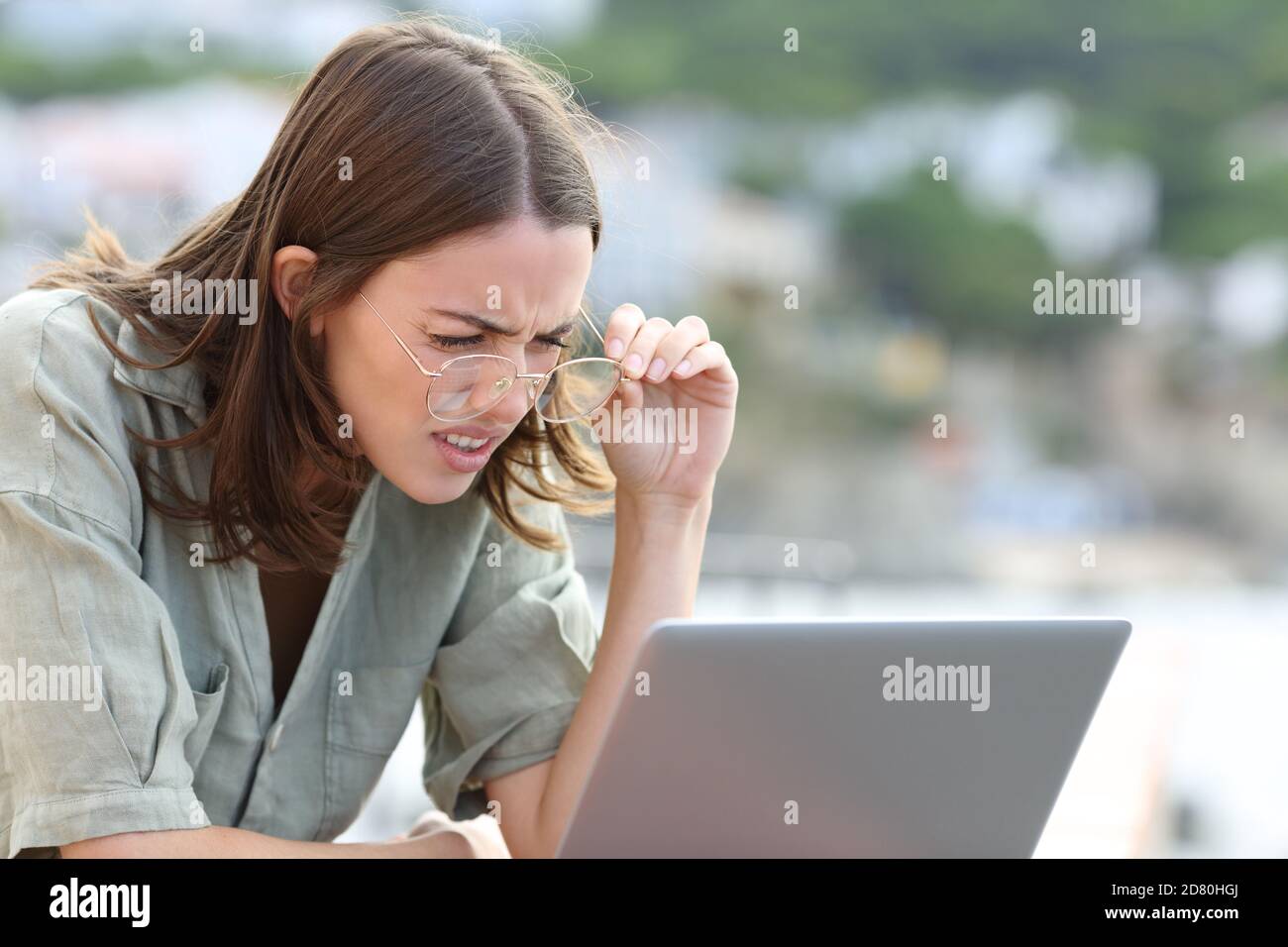 Stressed woman forcing sight wearing eyeglasees reading laptop outdoors Stock Photo