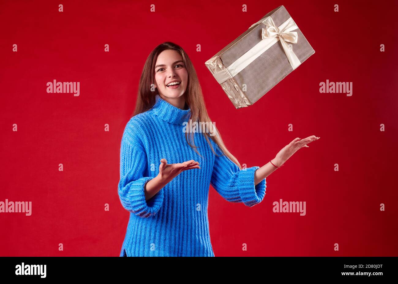 girl in a blue sweater catches gifts in the air on a red background. Stock Photo