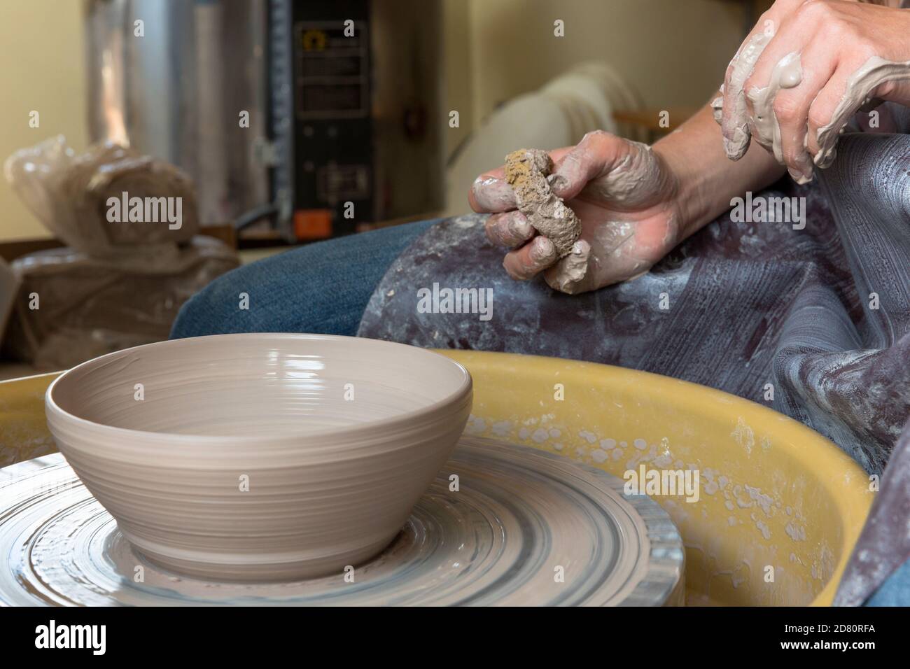 woman creating pottery at a potters wheel, hands covered in clay. Stock Photo
