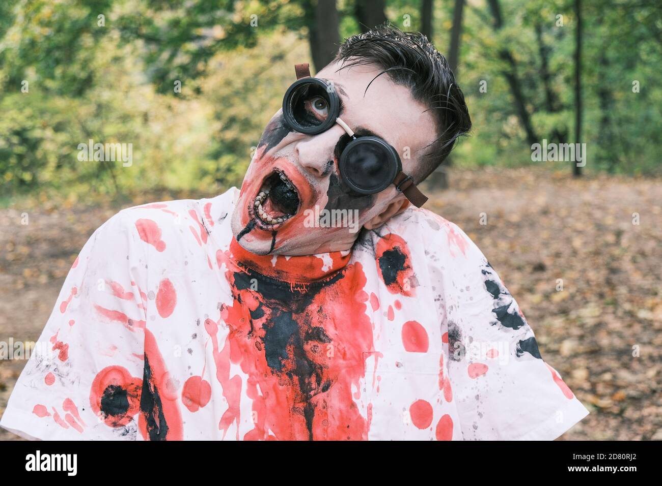 Horror, halloween and zombie concept. Portrait of an eerie man with zombie makeup with blood stains and black liquid in his mouth wriggles against bac Stock Photo