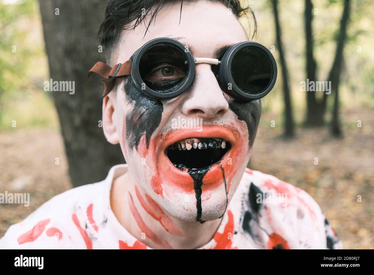 Horror, Halloween and zombie concept. Portrait of a creepy man in black glasses with zombie makeup with blood stains and black liquid in his mouth in Stock Photo