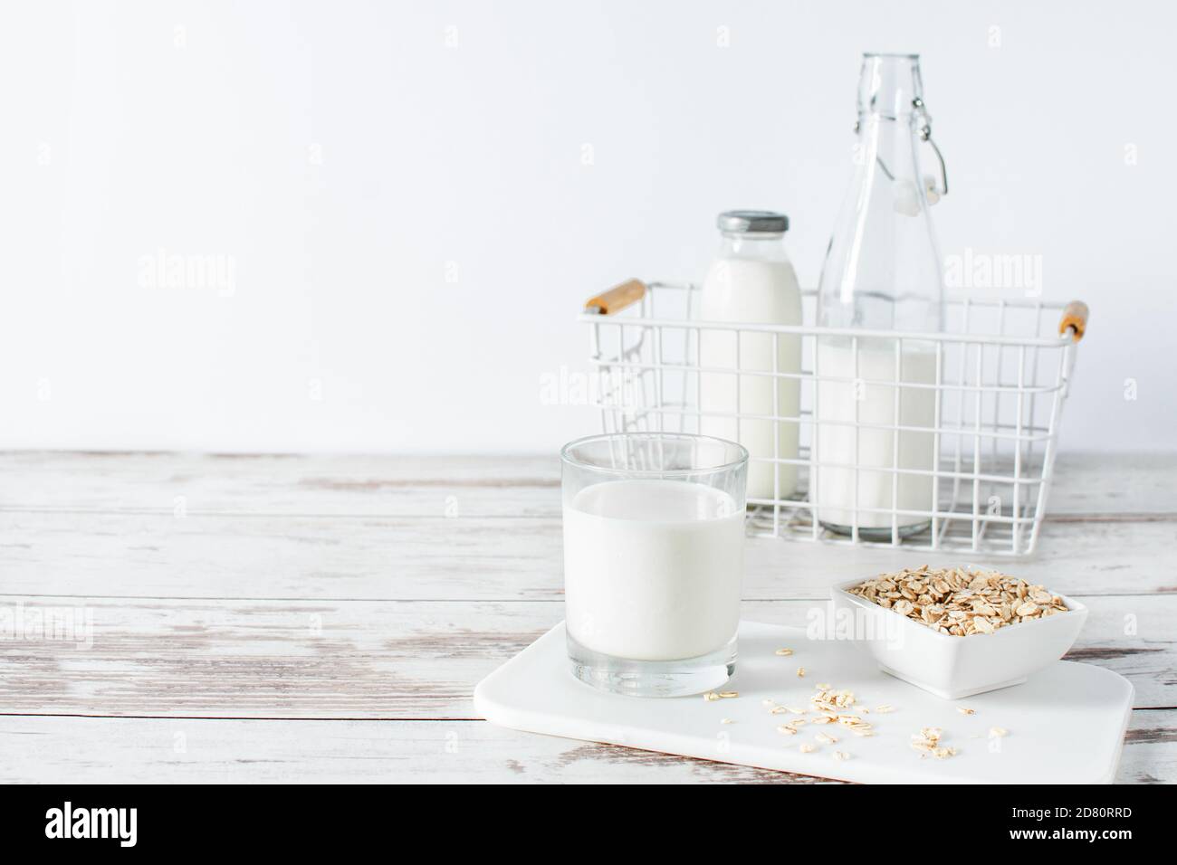 Homemade non dairy alternative milk made from oat flakes. Vegan oat milk on white wooden table. Stock Photo