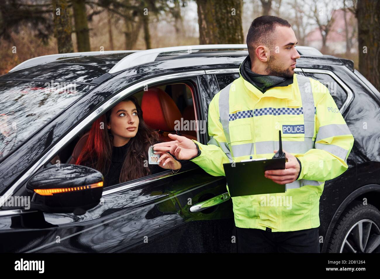 Male police officer in green uniform takes bribe from woman in car