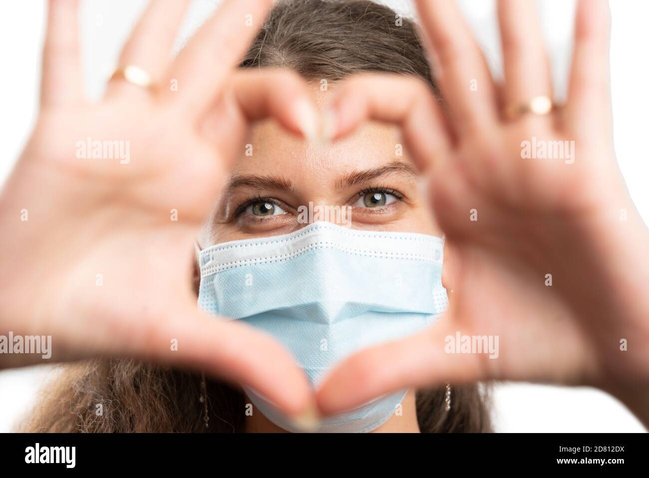 Close-up of adult woman model wearing medical or surgical disposable mask to prevent infection with covid19 sars influenza virus making heart love ges Stock Photo