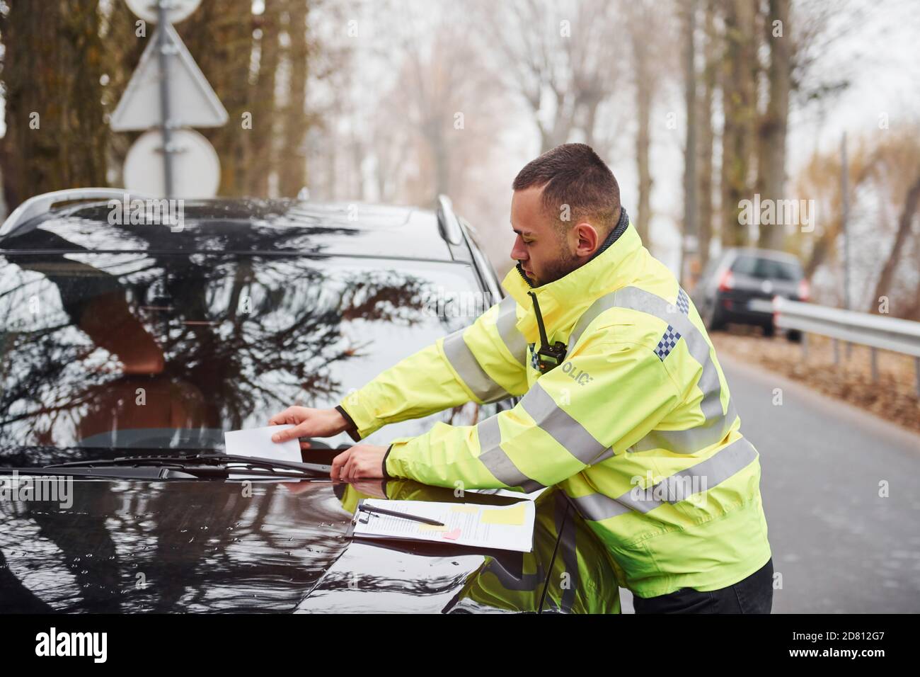 Male police officer in green uniform putting fine list to the vehicle