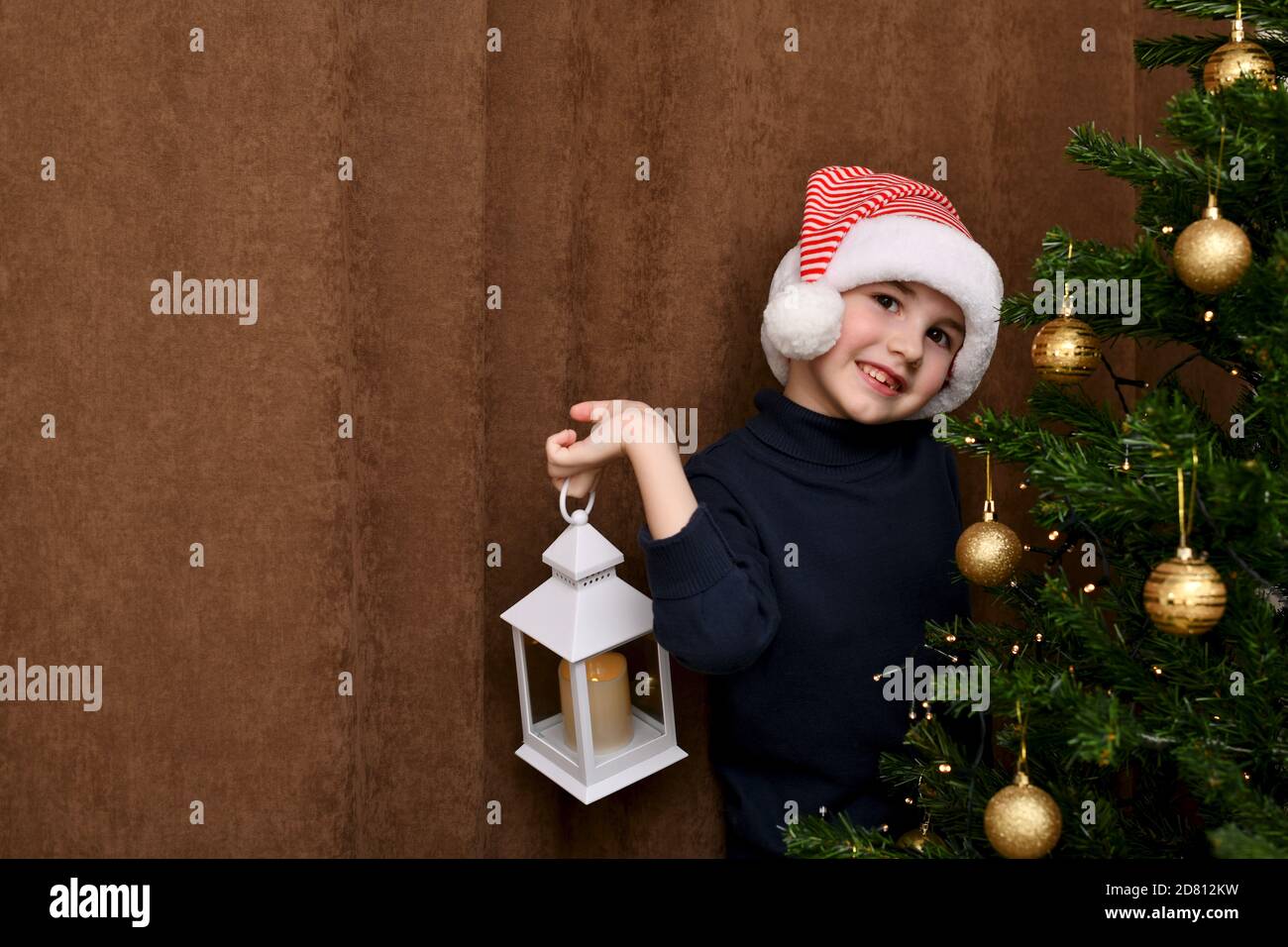 The child cheerfully imagines in his hand near the Christmas tree. Stock Photo