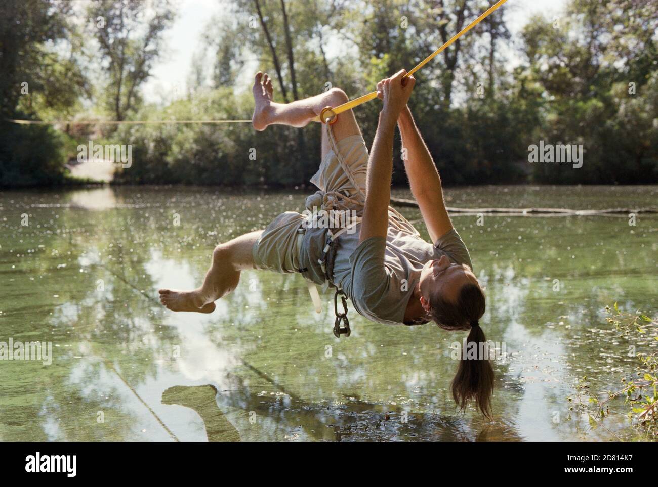A man practicing slackline over a river in the forest at sunset. Stock Photo
