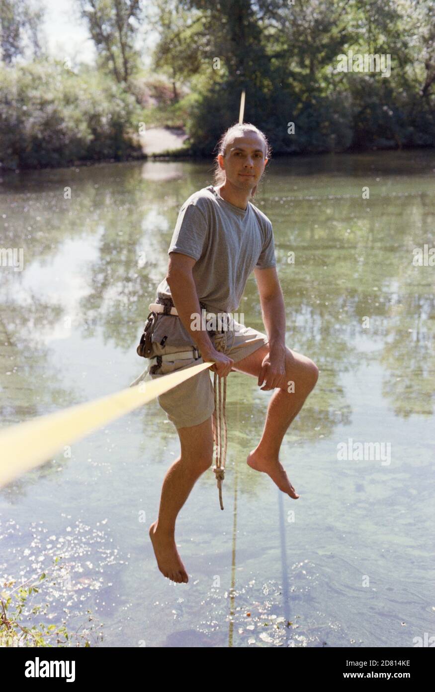 A man practicing slackline over a river in the forest at sunset. Stock Photo
