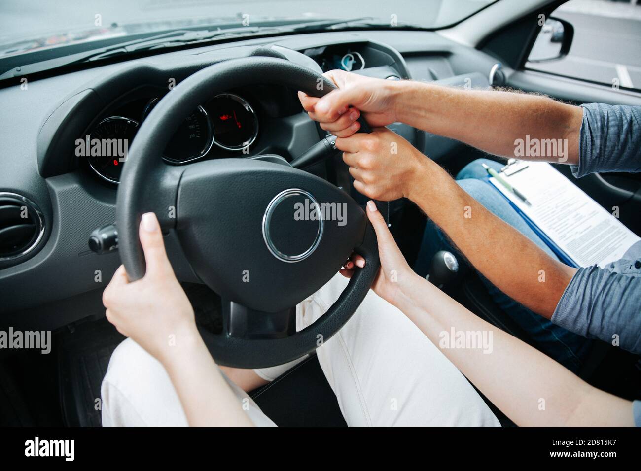 Two pairs of hands turn steering wheel together. Female student at