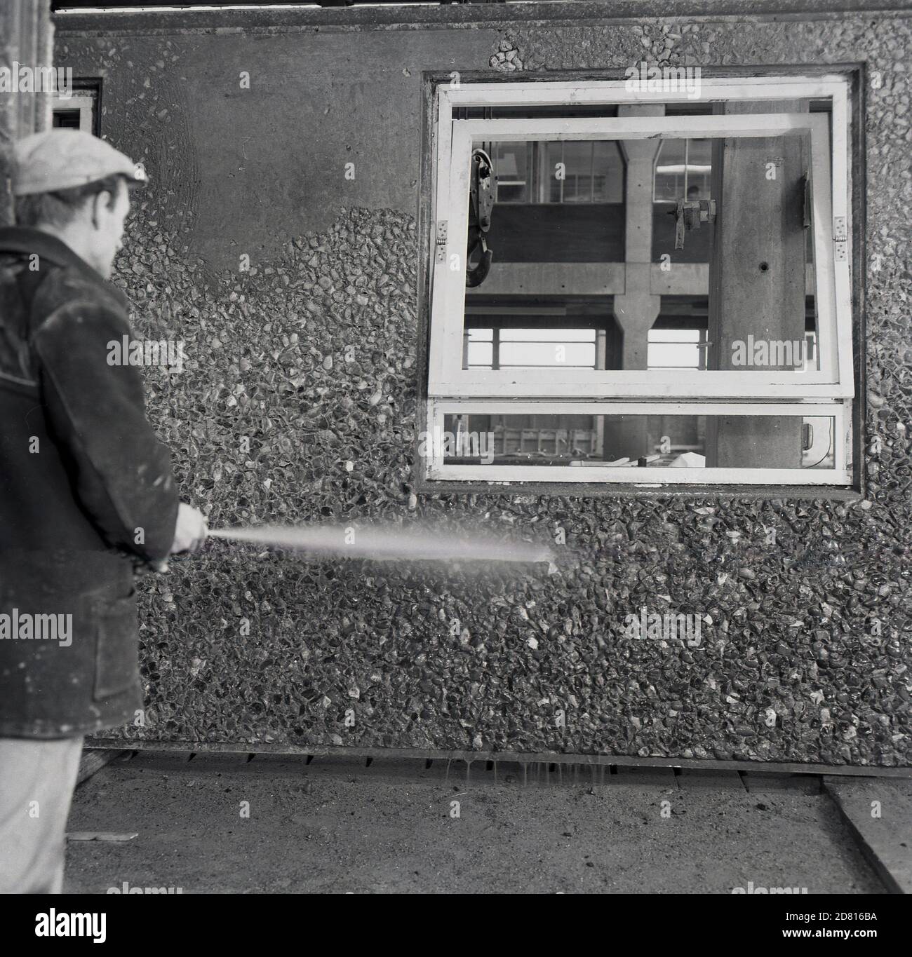 1960s, historical, a workman washing down a newly constructed precast concrete panel for external use, with a pebbledash exterior and built-in wooden windows, England, UK.  It was in this era that the precast concrete method of building modern offices and tower blocks became popular, as they could be built off-site and so reducing the need for large numbers of skilled workers and materials such as bricks, thereby reducing overall costs and speeding up the build. Stock Photo