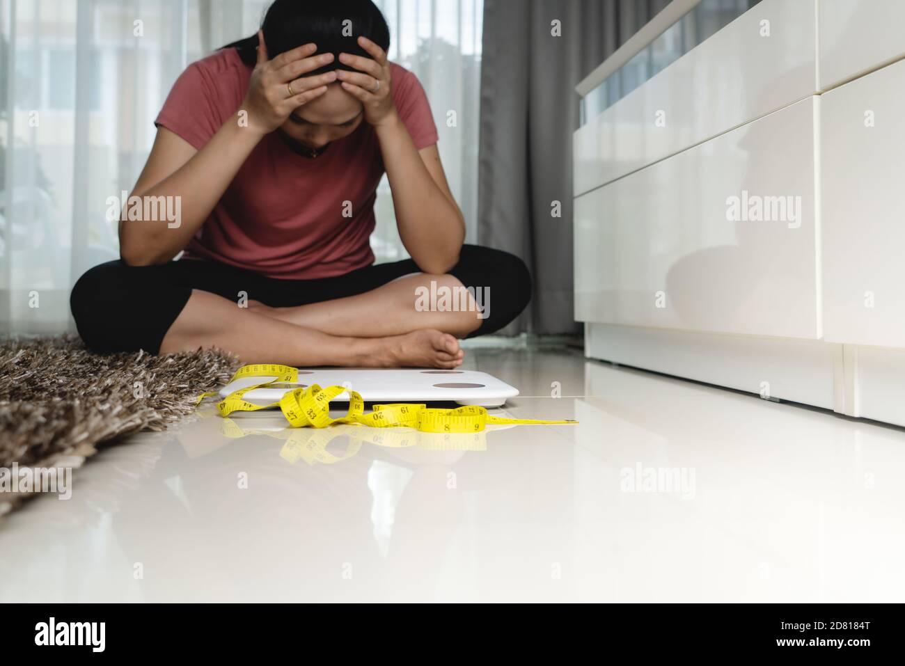 Weight loss fail concept. Scale and measure tape with depressed, frustrated and sad woman sitting on floor - soft focus on measure tape Stock Photo