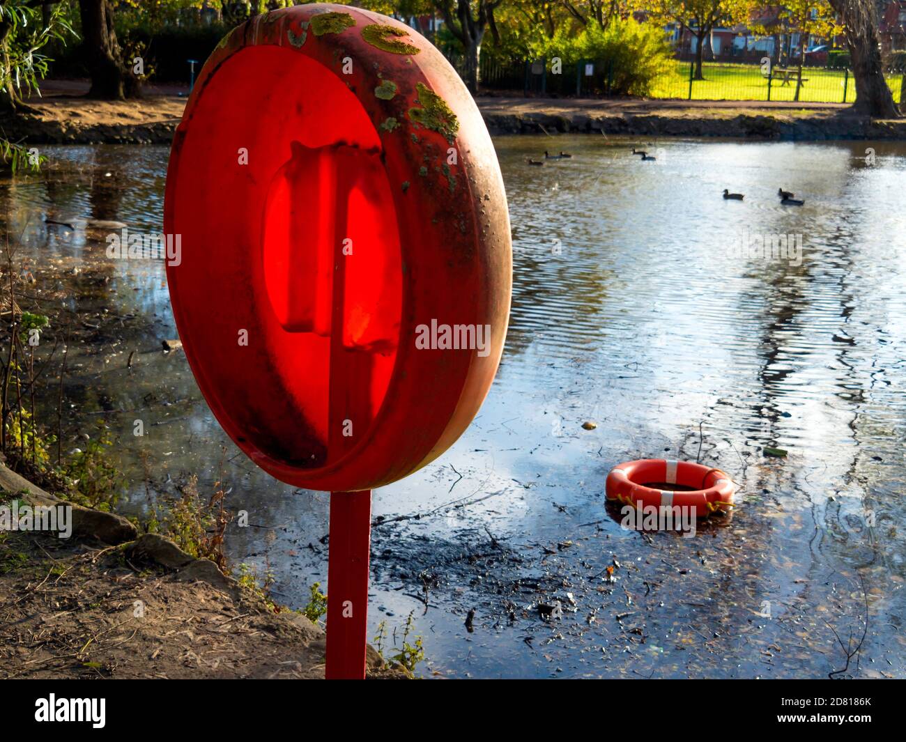 A lifebelt as a safety measure by a lake in a public park made useless by having been vandalized and thrown out of reach into the water Stock Photo