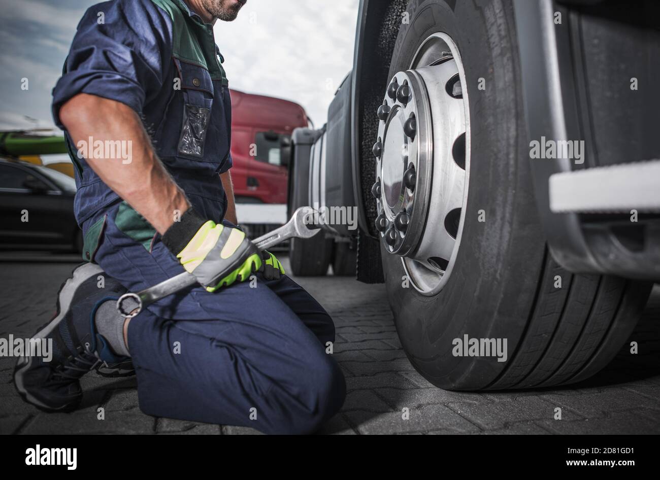 Caucasian Truck Mechanic with Large Wrench in His Hand Perform Scheduled Vehicle Maintenance. Looking on the Semi Truck Wheel and Tire. Stock Photo