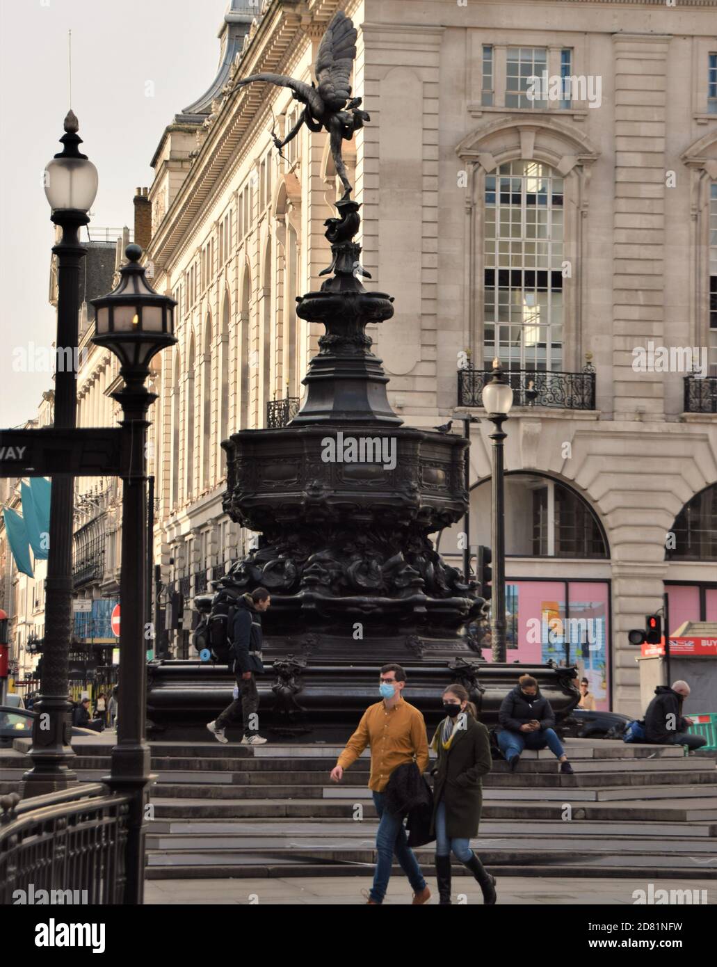 People with face masks walk past the Shaftesbury Memorial Fountain aka Eros, Piccadilly Circus, London Stock Photo