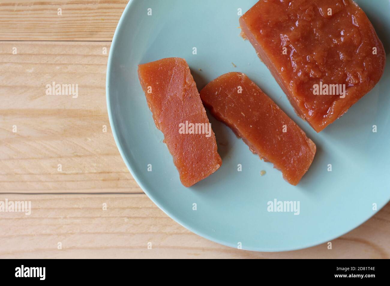 Top down view of home made Quince paste: Dulce de Membrillo. Sliced on a green plate on a wooden table, with copyspace to left. A sweet treat which is Stock Photo