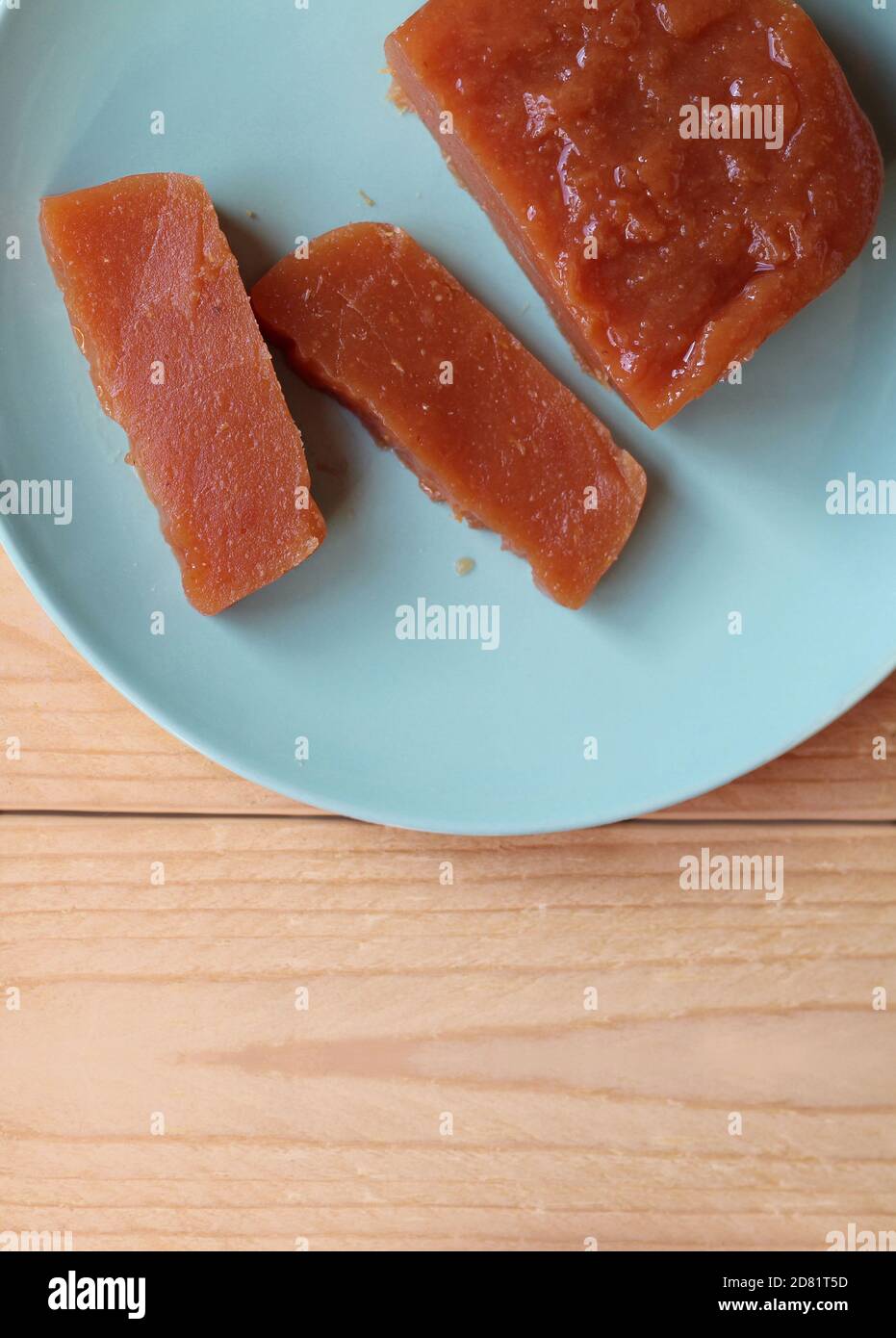 Top down view of home made Quince paste: Dulce de Membrillo. Sliced on a green plate on a wooden table, with copyspace below. A sweet treat which is a Stock Photo