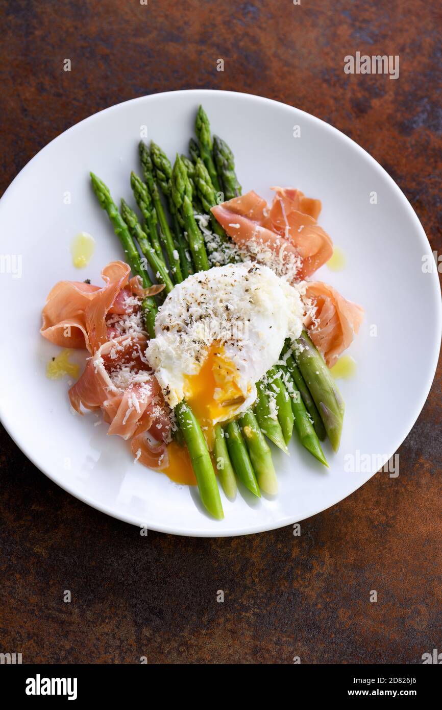 Eggs Benedict with parmesan, green asparagus and Parma ham. Stock Photo