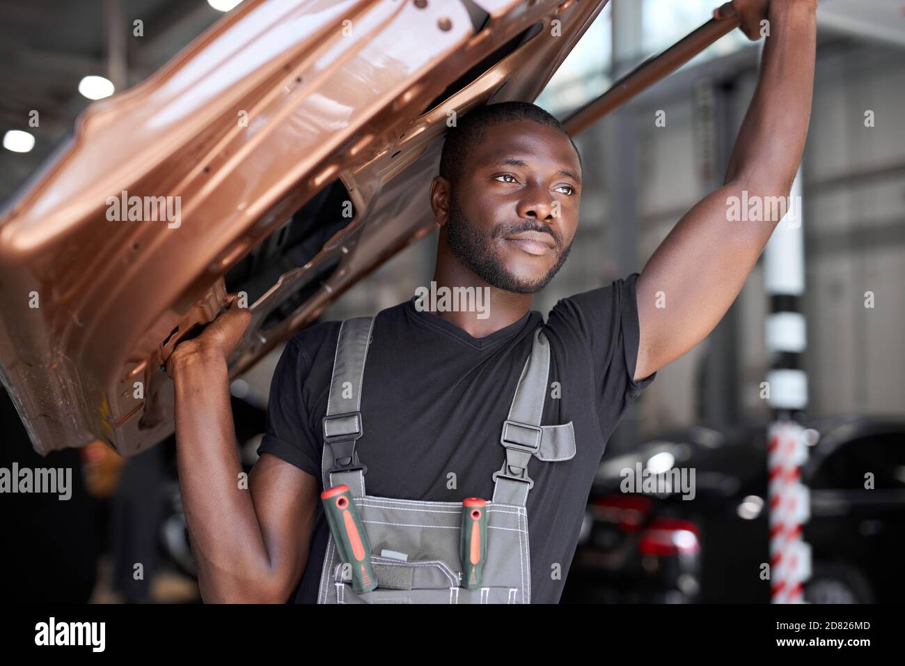 confident auto mechanic holding seperate part of the car, going to repair it at work place, hold it above head Stock Photo