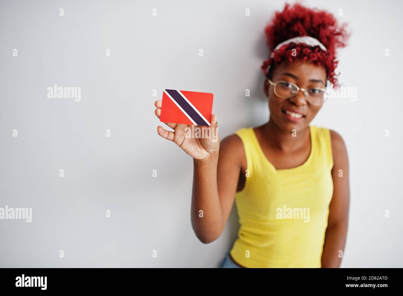 African american woman with afro hair, wear yellow singlet and eyeglasses, hold Trinidad and Tobago flag isolated on white background. Stock Photo