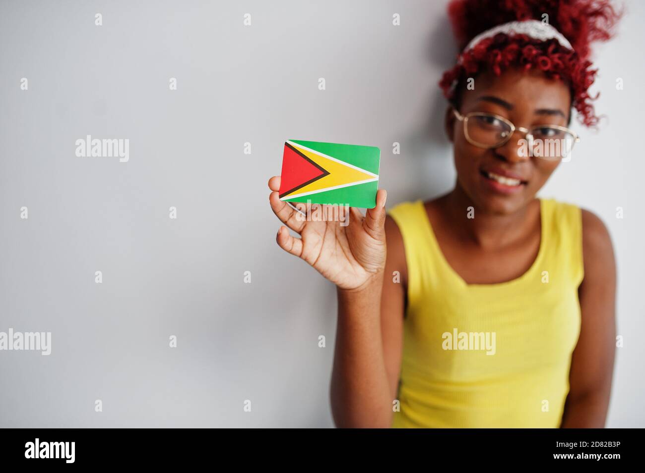 African american woman with afro hair, wear yellow singlet and eyeglasses, hold Guyana flag isolated on white background. Stock Photo