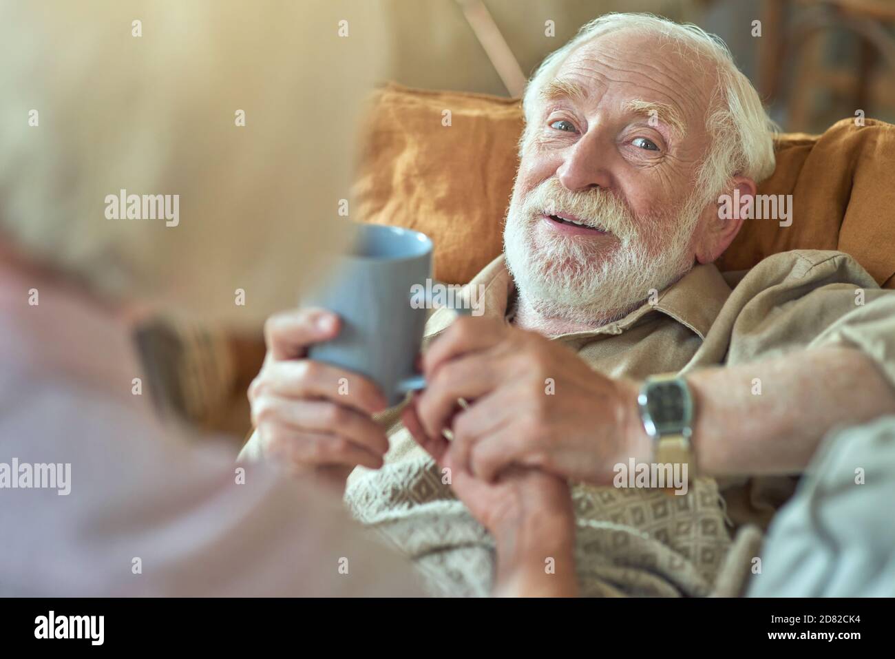 Cropped photo of careful senior woman giving cup of hot drink for her husband during his illness at home. Care and health concept Stock Photo