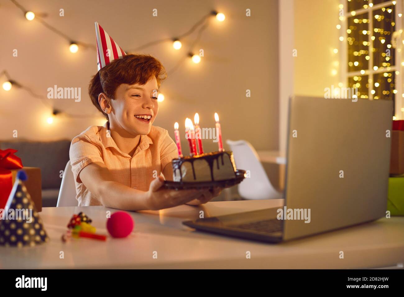 Happy boy sitting at laptop computer and having online birthday party with friends or relatives Stock Photo