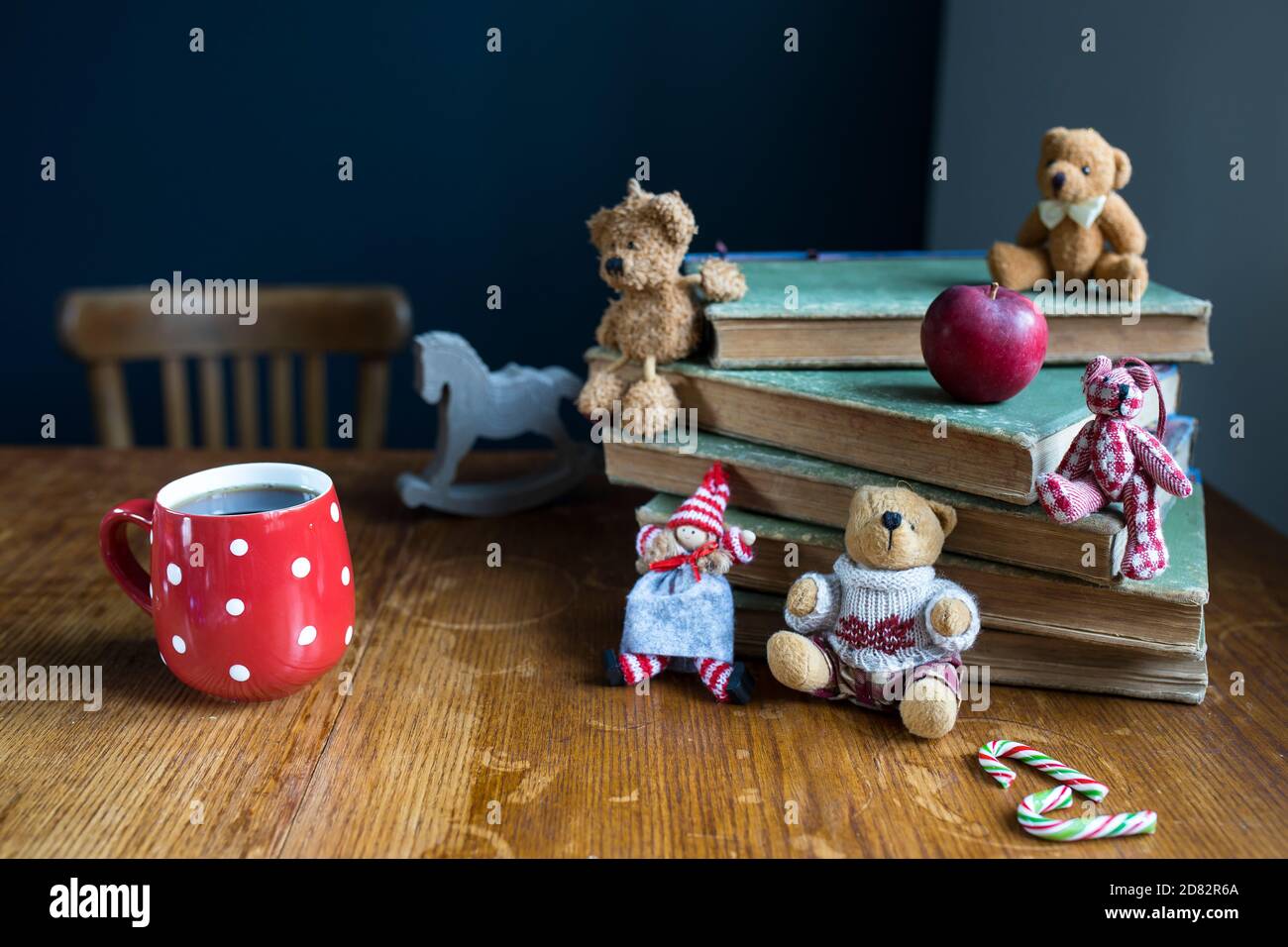 A Christmas doll and bears sit on a stack of old books. Copy space. Selective focus. Red cup with white polka dots with tea. Stock Photo