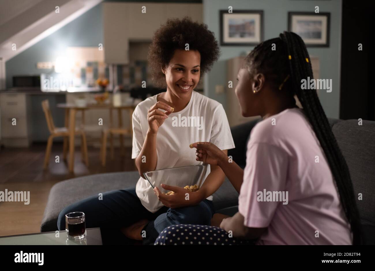 Young multiethnic women in pajamas sitting on sofa with popcorn and talking  enjoying sleepover party in evening Stock Photo - Alamy
