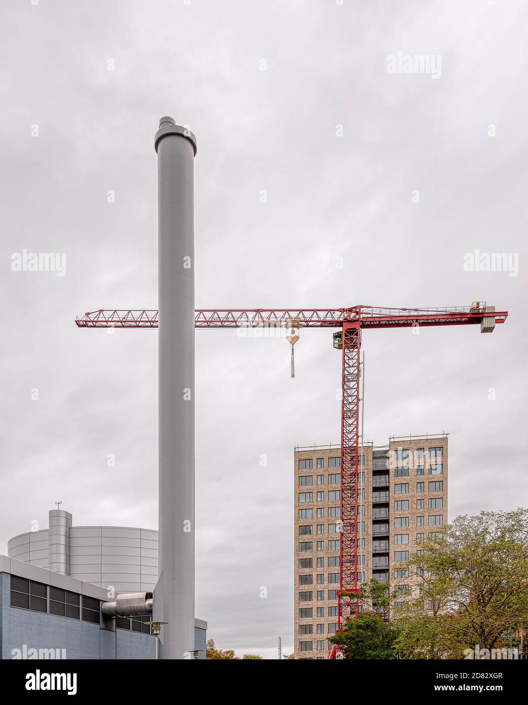 apartment block behind a heating plant chimney with a red construction-crane, Frederikssund, Denmark, October 25, 2020 Stock Photo