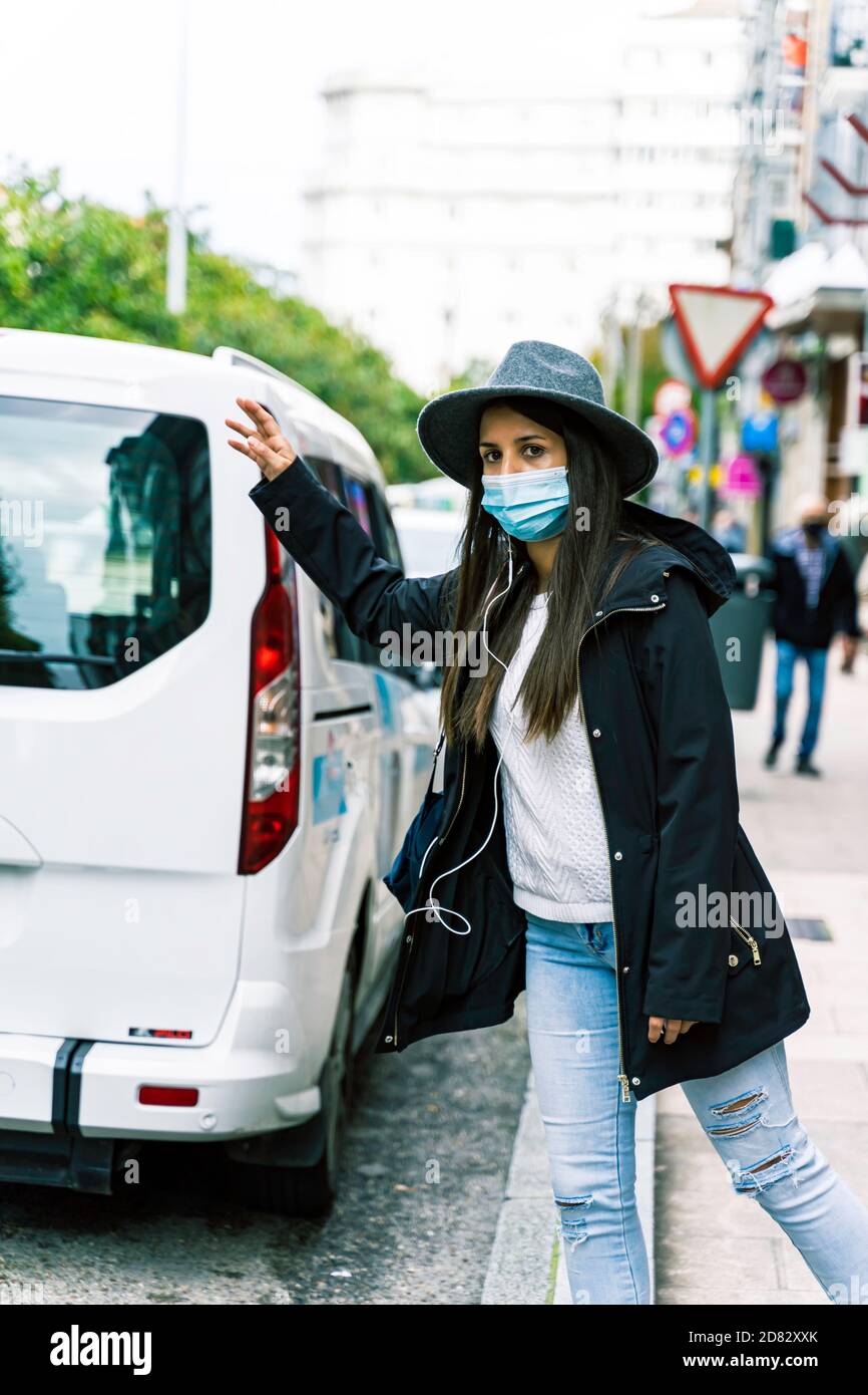young woman in the city wearing face mask and hailing a taxi cab Stock