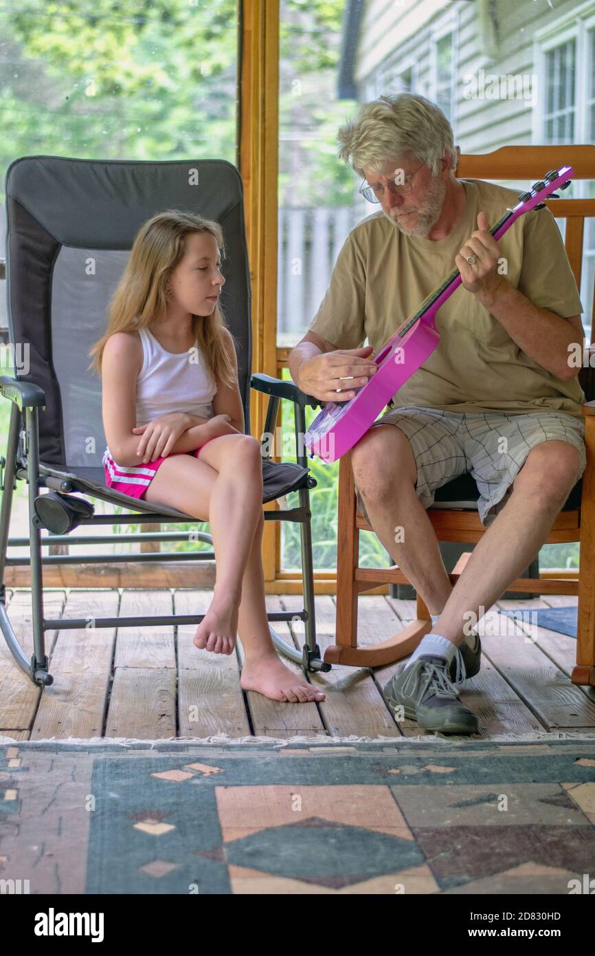 Grandfather demonstrates how to strum a guitar on this young girls new pink instrument Stock Photo