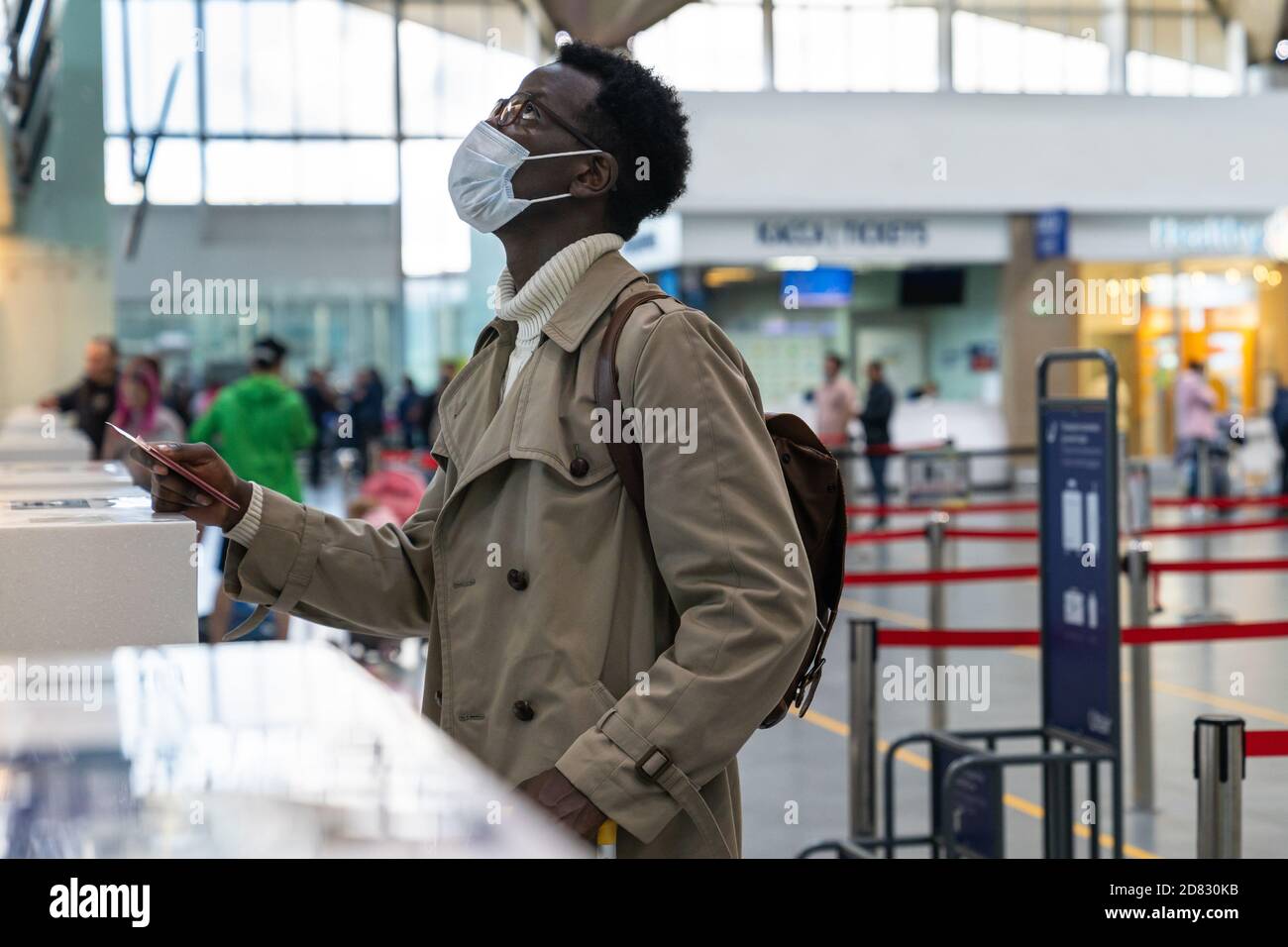 African American man stands at check-in counters at the airport terminal, giving passport to an officer. Flight rules during a Covid-19 pandemic only Stock Photo