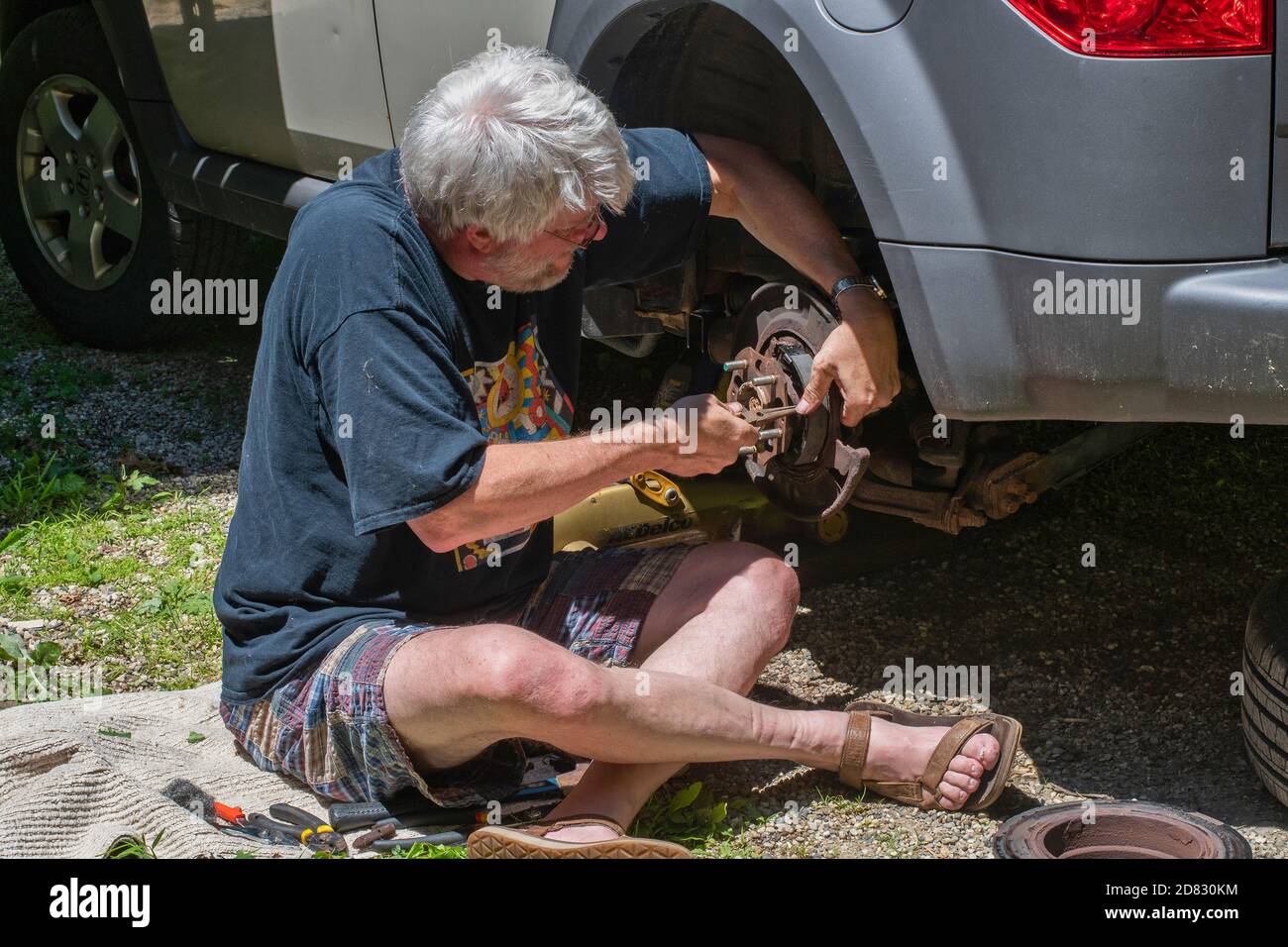 A senior male becomes a drive way mechanic as he saves money by repairing his brakes himself at home Stock Photo