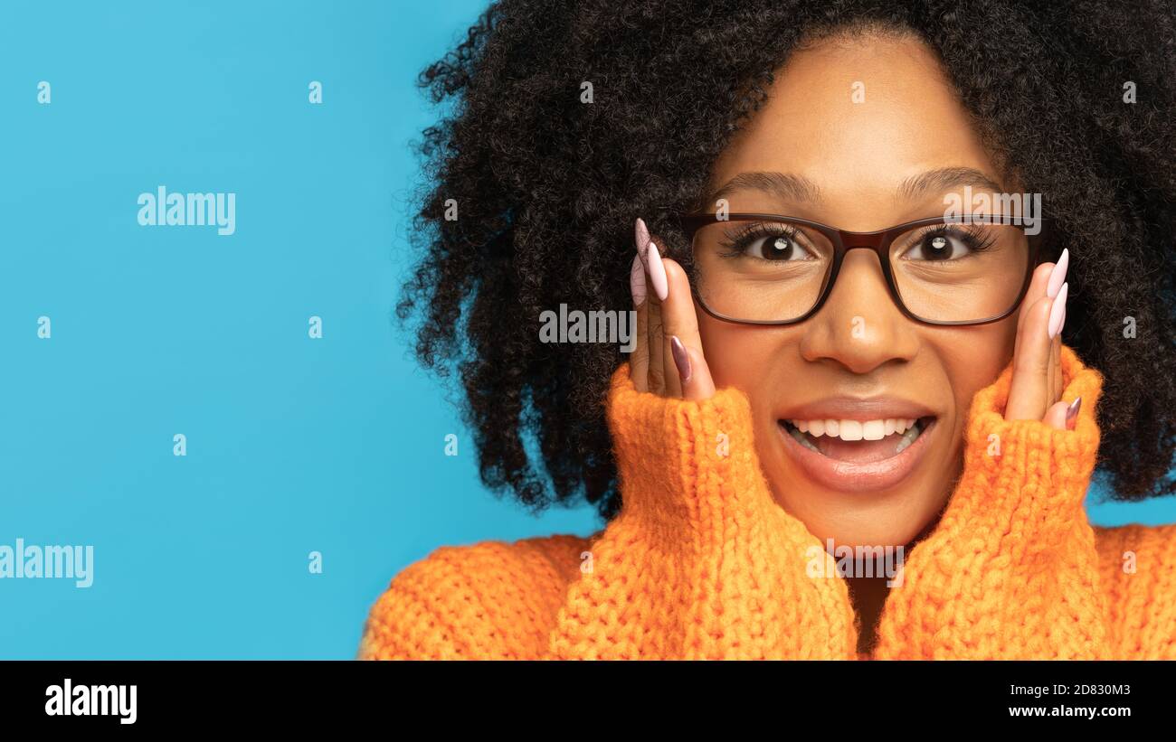 Surprise biracial woman in orange jumper surprise holding cheeks by hands. Mixed race woman wear glasses with clean fresh skin looking at camera, isol Stock Photo