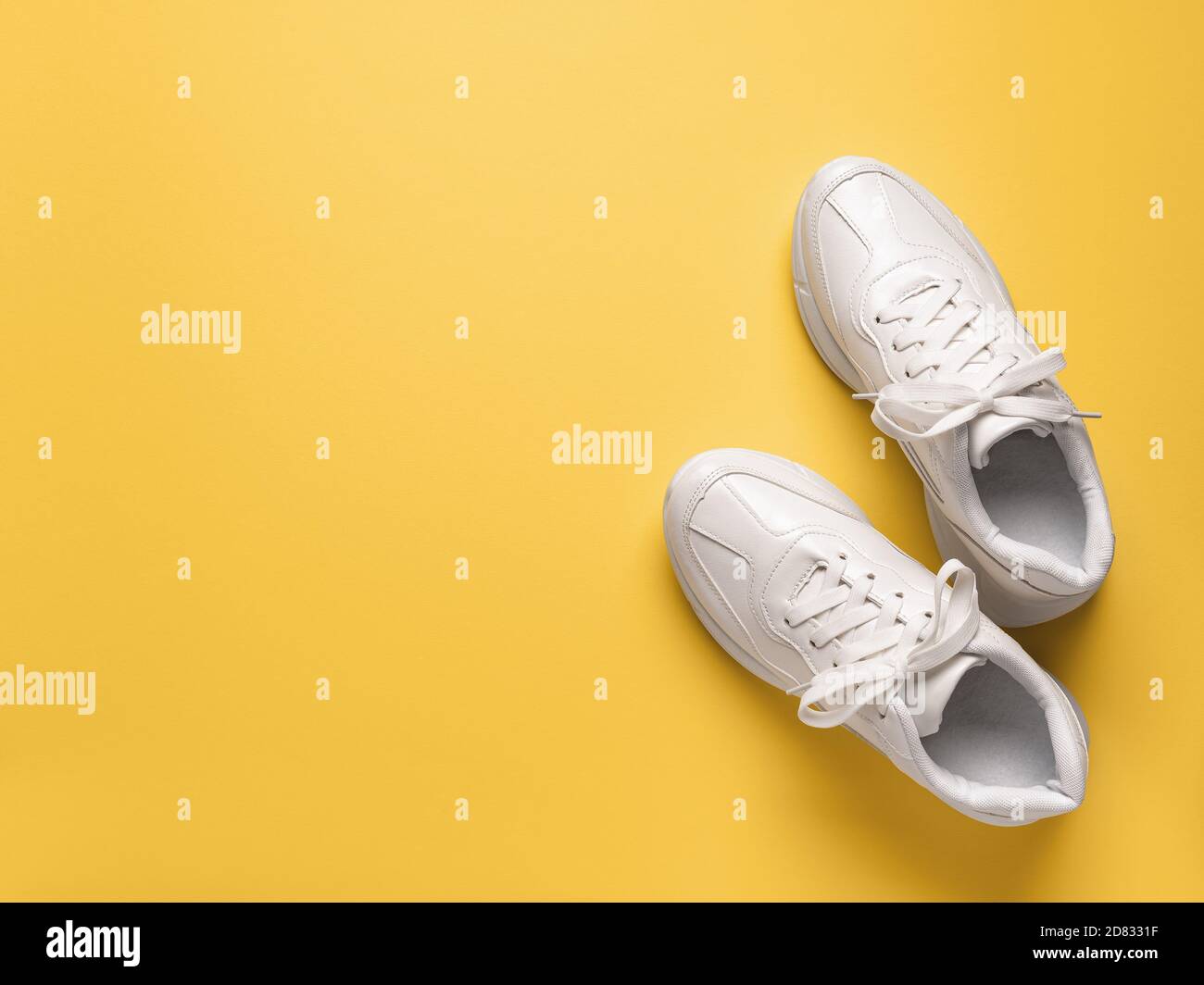 Pair of white chunky sole sneakers over an yellow amber paper background. New unisex tied laces